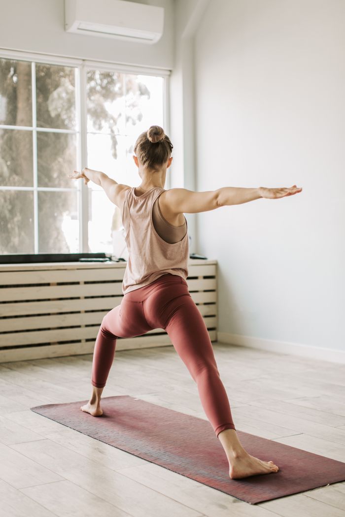 Offerings A young woman performs a warrior pose during a yoga session in a bright indoor space.